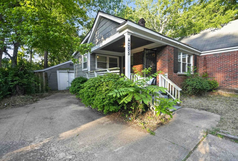 Brick and siding exterior featuring a covered front porch with white railing, a concrete driveway, and established landscaping