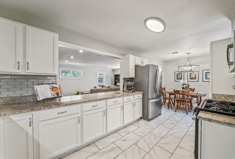 Kitchen featuring white cabinetry, light-toned granite countertops, a subway tile backsplash, and large format tile flooring