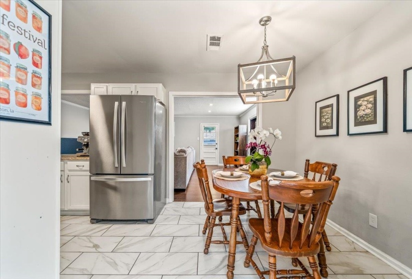 Kitchen and dining area featuring white cabinetry, stainless steel refrigerator, white tile flooring, and a decorative ceiling light fixture