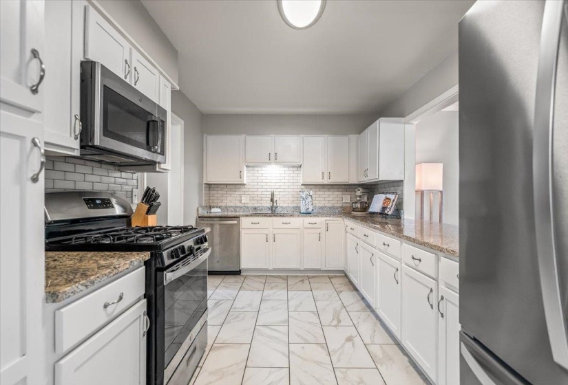Kitchen featuring white cabinetry, subway tile backsplash, stainless steel appliances, granite countertops, and tile flooring