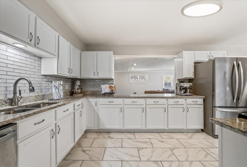 Kitchen featuring white cabinetry, light-toned countertops, a subway tile backsplash, stainless steel appliances, and large format tile flooring