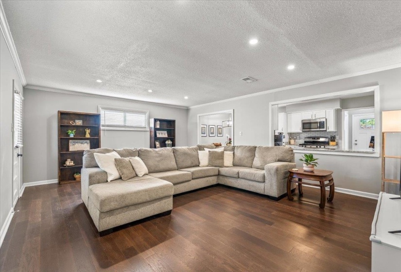Spacious living area featuring rich wood-finish flooring, recessed lighting, and crown molding
