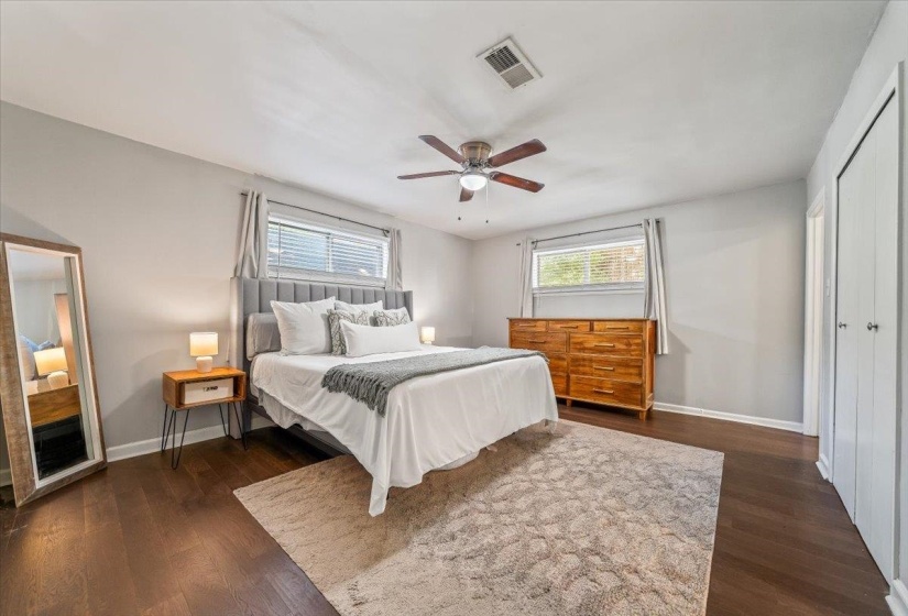 Bedroom featuring dark wood-finish flooring, light gray walls, a ceiling fan with light fixture, and two windows with blinds