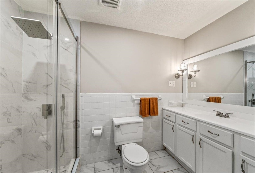 Contemporary bathroom featuring a spacious glass-enclosed shower with a rainfall showerhead, white marble-look tile, and a double vanity with ample storage