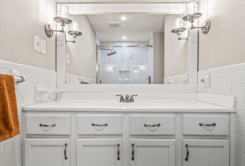 White vanity with integrated sink, brushed nickel faucet, mirror, and two wall-mounted light fixtures