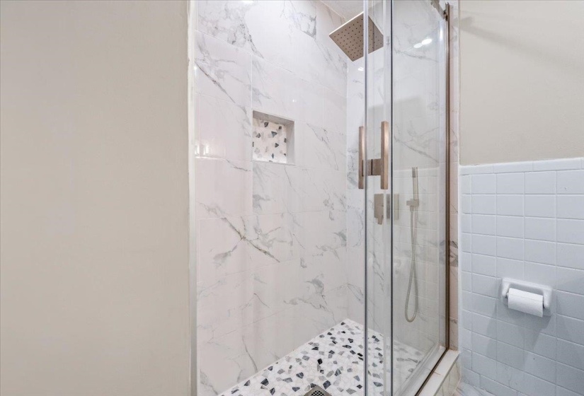 Glass-enclosed shower featuring white marble-patterned tile, a built-in shower bench with mosaic tile, a recessed niche with mosaic tile, and a rainfall showerhead