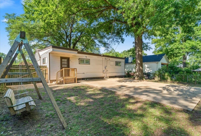 Spacious backyard featuring a large paved area, mature trees, and a wooden fence