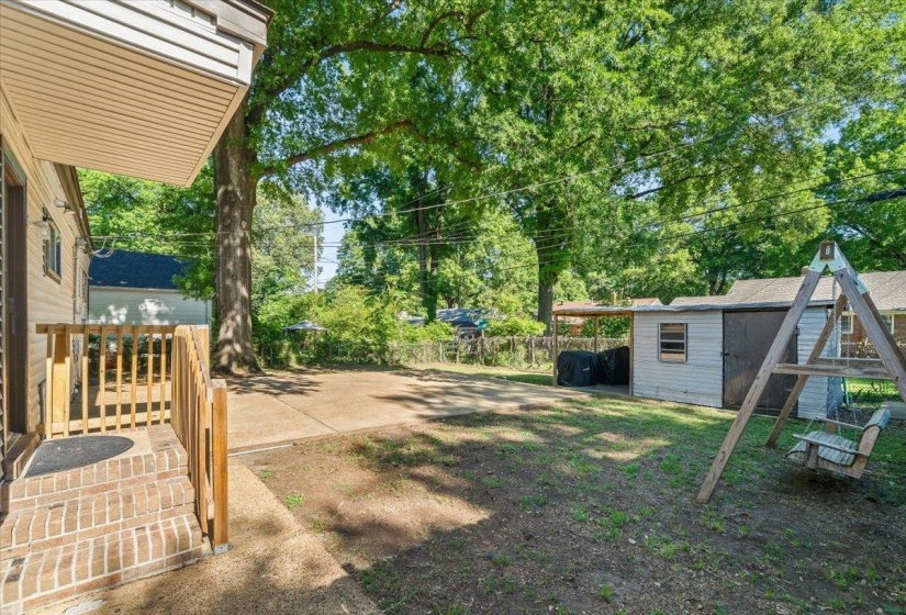 Expansive backyard featuring a large paved patio, mature trees, a storage shed, and an additional covered outdoor area
