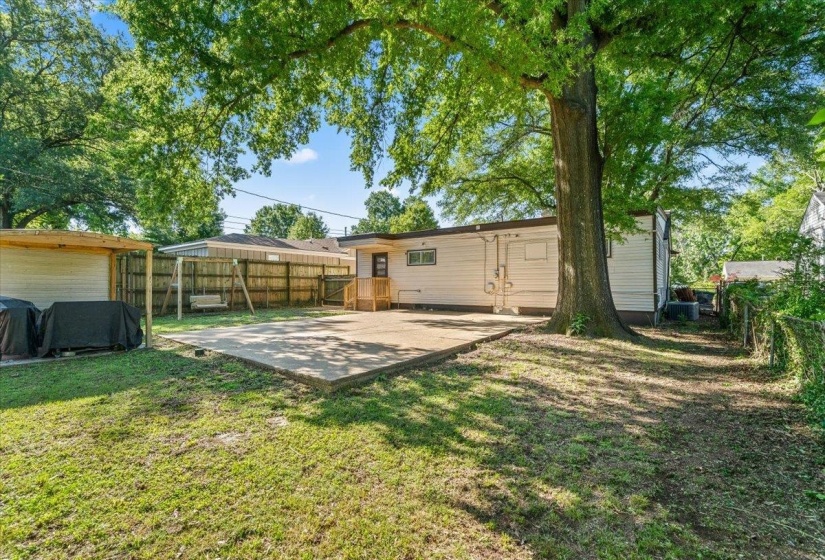 Expansive backyard featuring a concrete patio, mature trees, a wood privacy fence, and a covered patio area