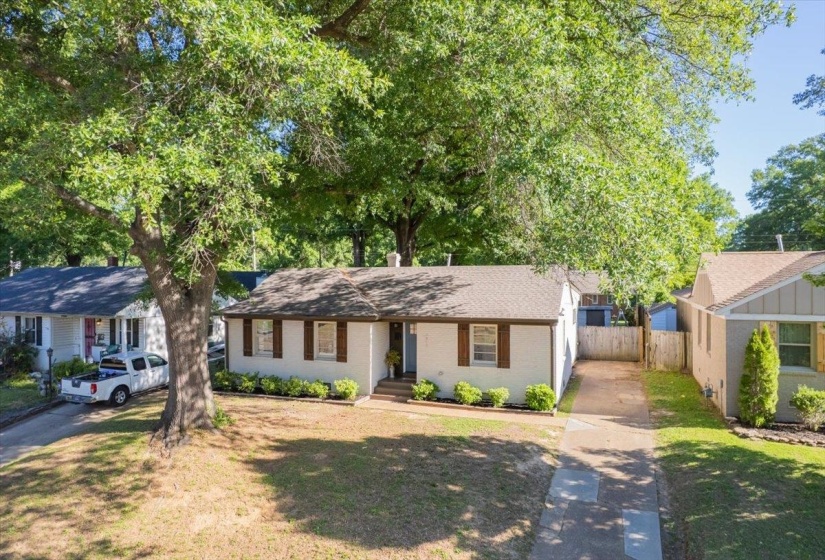 White brick exterior with brown shutters, a gabled roof, and a mature tree providing natural shade
