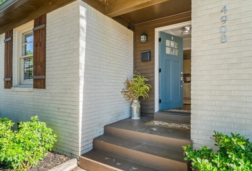 White brick exterior with natural wood shutters, a blue front door with glass lites, a covered porch with recessed lighting, and dark wood siding accents