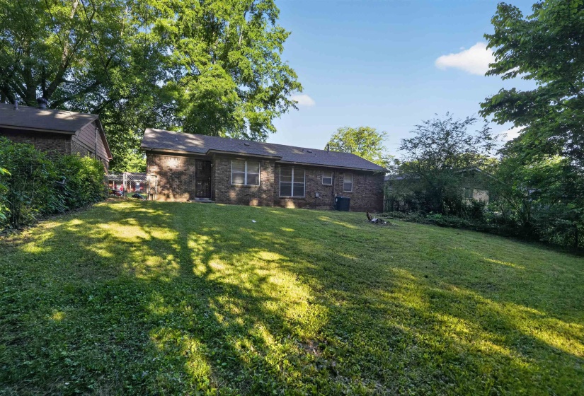Expansive grassy yard with mature trees providing partial shade