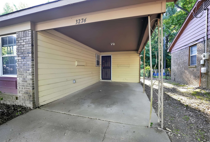 Covered concrete carport with decorative metal support columns, a light-colored siding exterior, and a brick facade accent