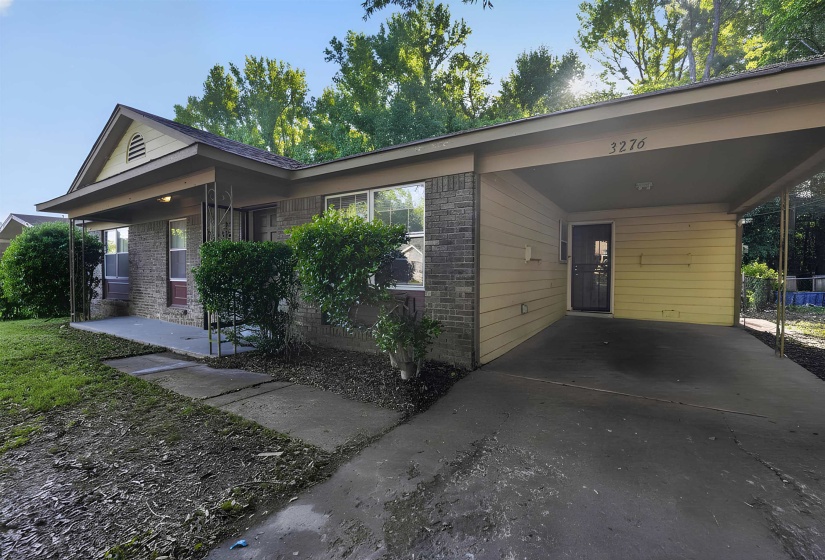 Exterior featuring a brick facade, covered front porch, and a carport