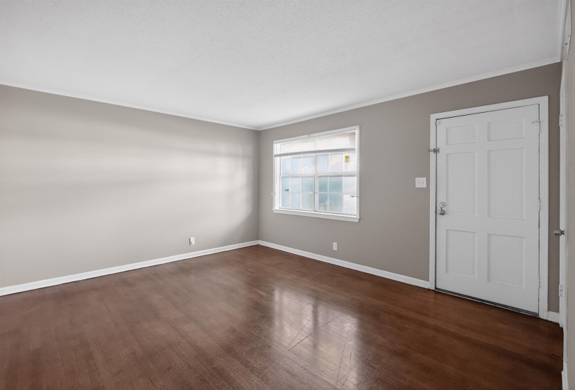 Spacious room featuring wood-finish flooring, light grey wall paint, white baseboards, and a paneled white door