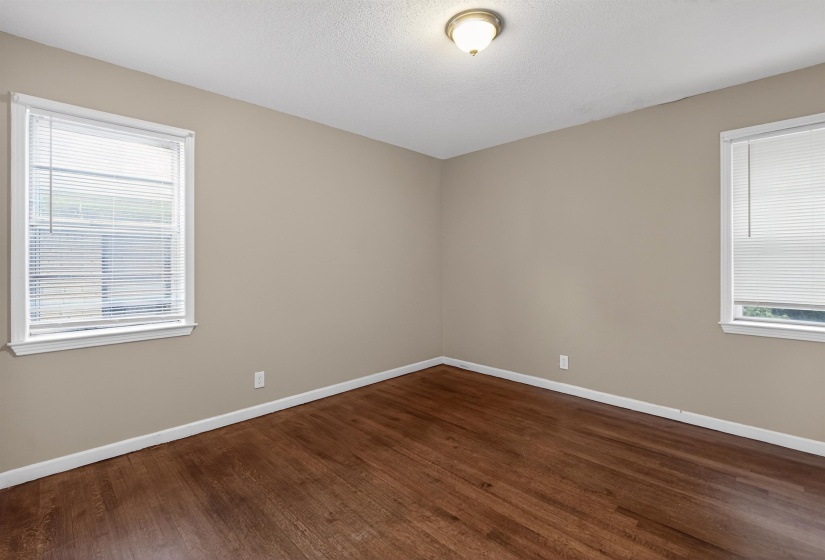 Interior space featuring wood-finish flooring, two windows with blinds, neutral-toned walls, and a ceiling-mounted light fixture
