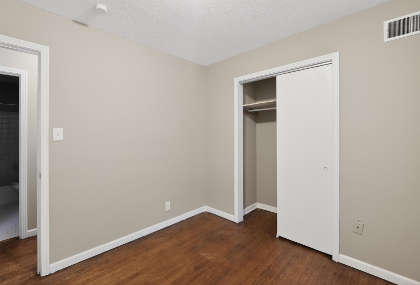 Room featuring wood-finish flooring, neutral wall paint, white baseboards, and a sliding closet door with built-in shelving and a clothing rod