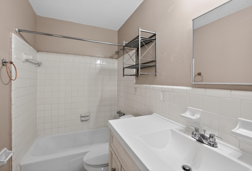 Bathroom featuring a white tiled shower/tub combination, single vanity with integrated sink, chrome faucet, and rectangular wall mirror