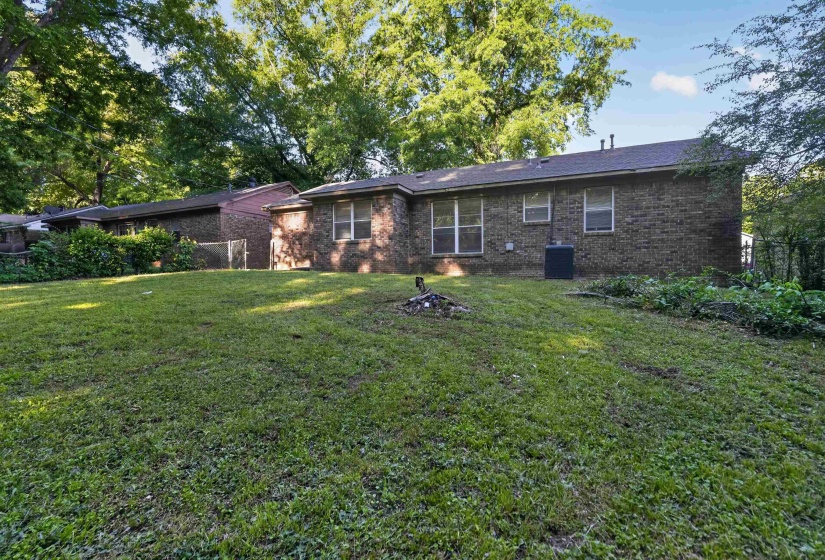 Expansive green lawn with a brick exterior home featuring multiple windows, a dark shingle roof, and established trees