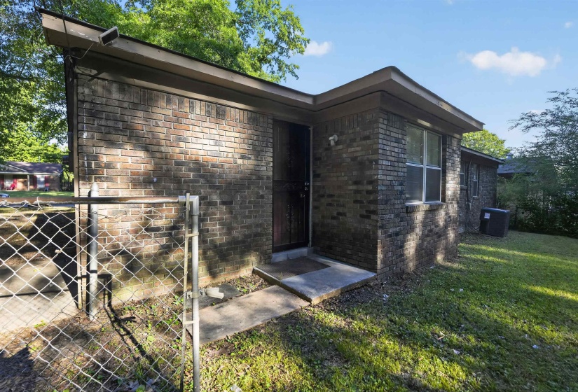 Brick exterior with a chain-link fence, concrete entryway, and mature landscaping