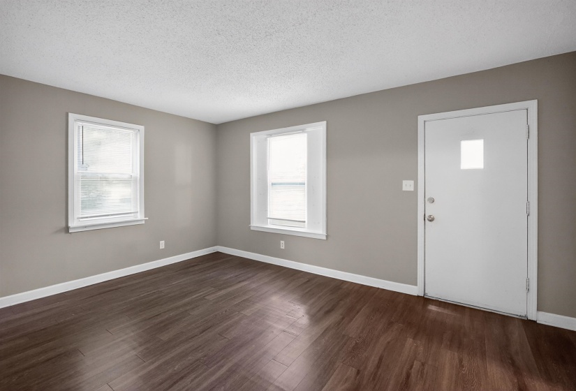 Spacious room featuring wood-finish flooring, neutral gray walls, white trim, and two double-hung windows