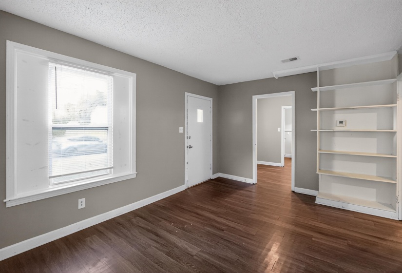 Living space featuring wood-finish flooring, neutral wall tones, and a large window with blinds