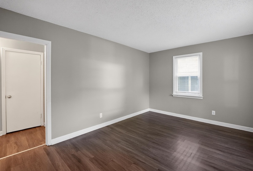 Spacious room featuring wood-finish flooring, light gray wall paint, white trim, and a window with blinds