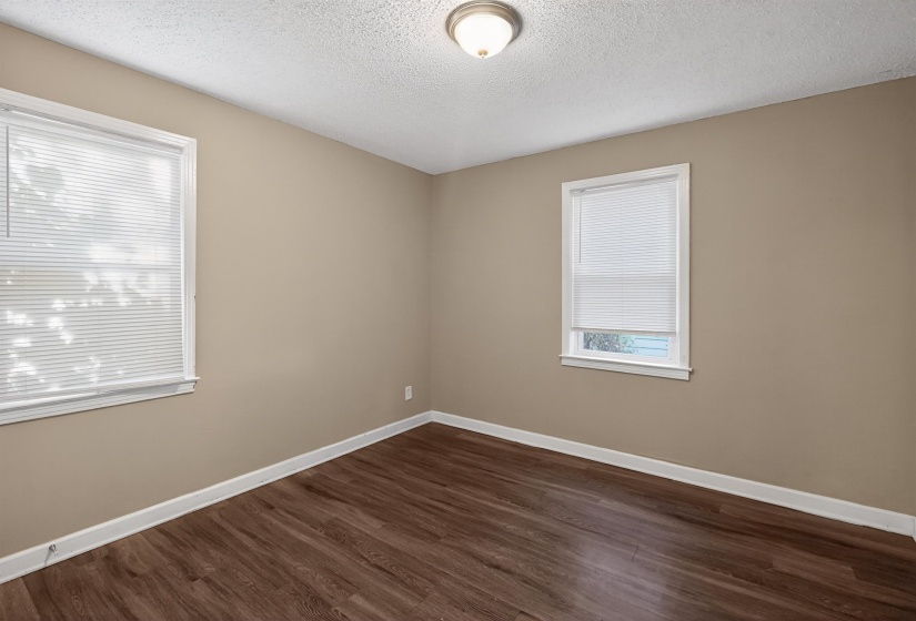 Interior room featuring wood-finish flooring, two windows with white blinds, a neutral wall color, white trim, and a ceiling-mounted light fixture