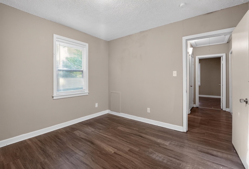Spacious room featuring wood-finish flooring, neutral-toned walls, a single window with blinds, and white trim throughout