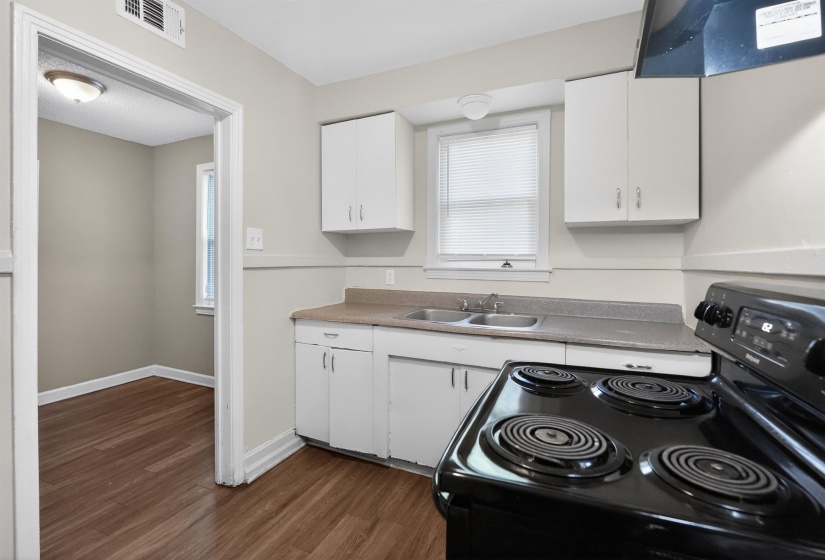 Kitchen featuring wood-finish flooring, white cabinetry, laminate countertops, and a black electric range