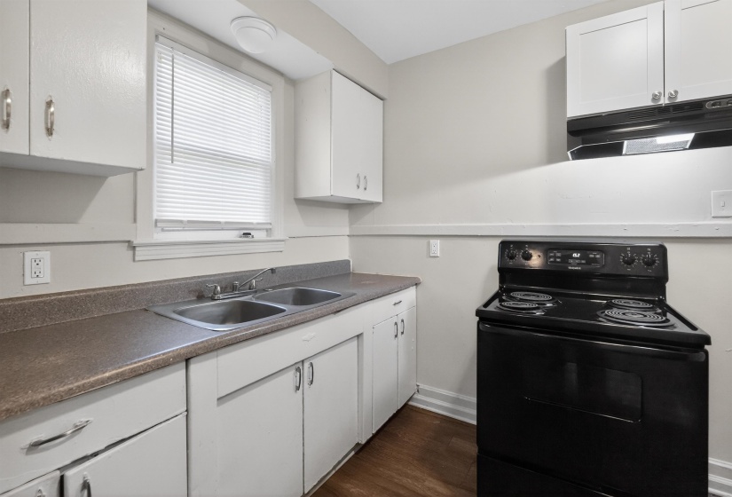 Kitchen featuring white cabinetry, a double basin stainless steel sink, a black electric range with an overhead vent hood, and wood-finish flooring