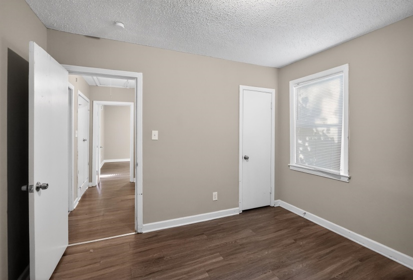 Interior room featuring wood-finish flooring, neutral wall paint, white trim, and a window with blinds