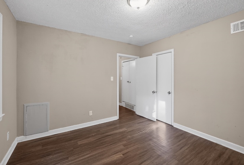 Room featuring wood-finish flooring, neutral wall paint, white trim, and two white bi-fold closet doors