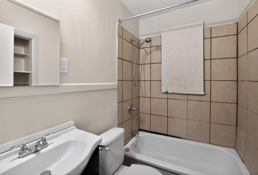 Bathroom featuring a white bathtub, ceramic tile surround, wall-mounted shower head with handheld attachment, and a medicine cabinet with open shelving