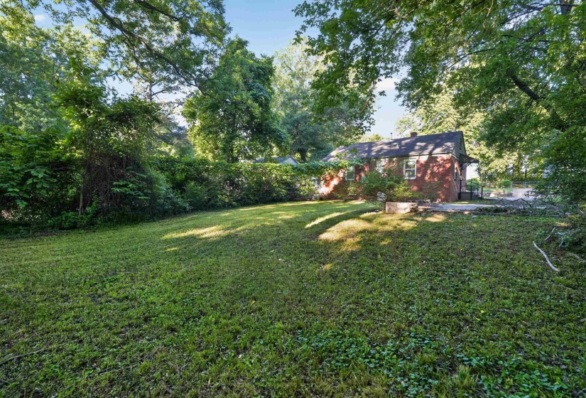 Expansive backyard with a manicured lawn, established trees, and a brick exterior residence