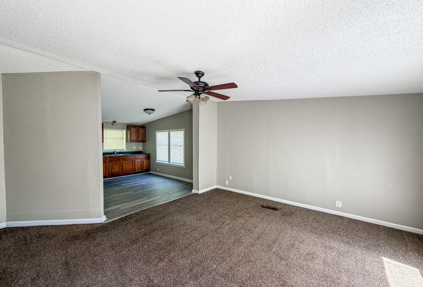 Living area featuring textured carpeting, neutral wall finishes, and a ceiling fan with integrated lighting