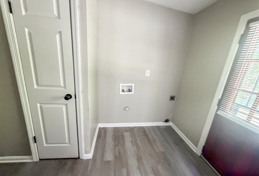Laundry area featuring wood-finish flooring, light grey painted walls, and white baseboards