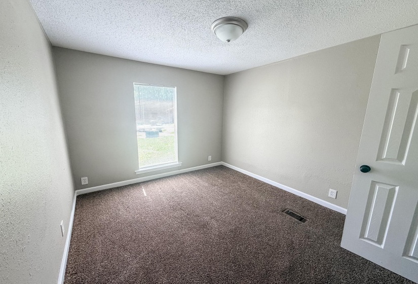 Neutral-toned room featuring brown carpet flooring, a single window with blinds, and a white paneled door