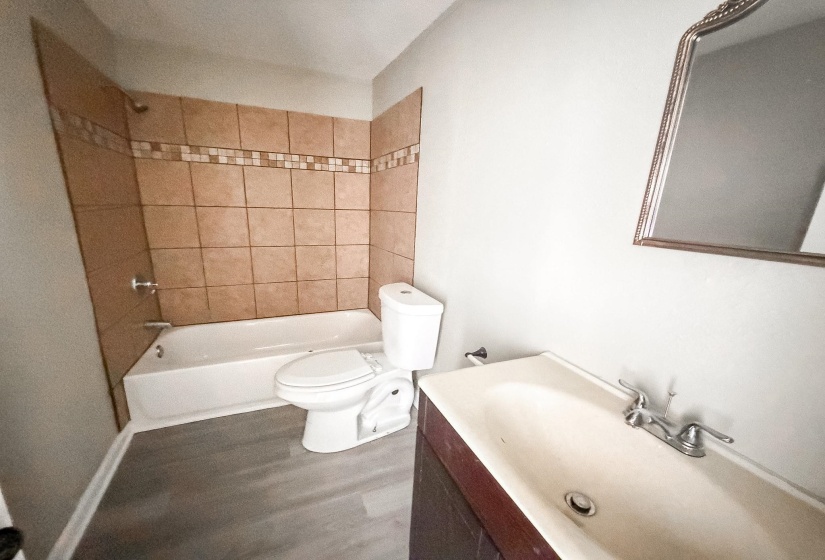 Bathroom featuring a combination bathtub and shower with brown tile surround and mosaic accent strip