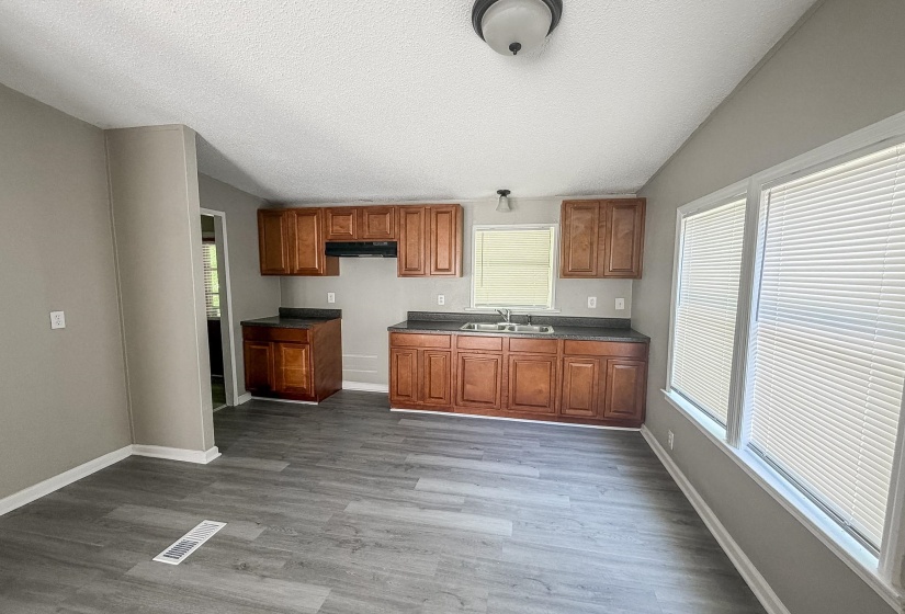 Kitchen area featuring wood-finish cabinetry, dark countertops, a double basin sink, and a window above the sink
