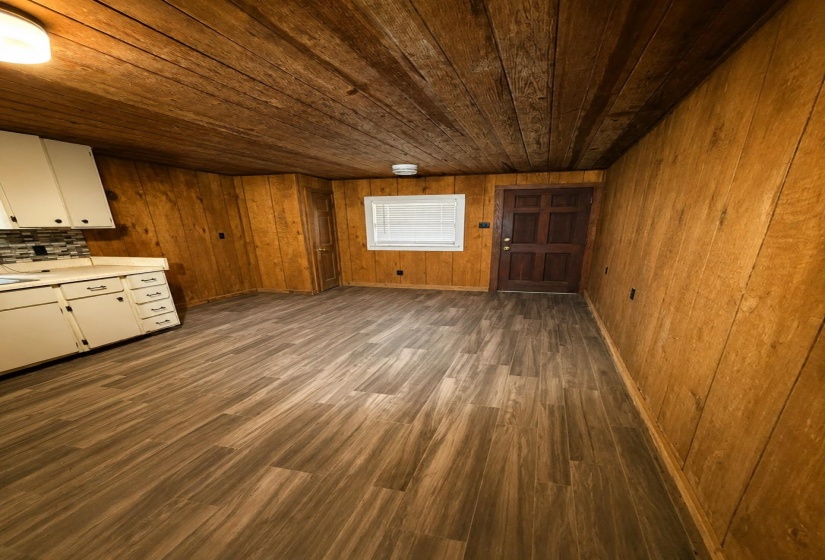 Open-concept room featuring wood-finish flooring, wood paneling on walls and ceiling, white cabinetry, and a tile backsplash