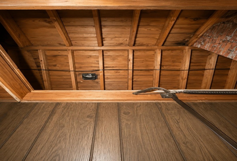 Attic space featuring exposed wood beams, finished wood planking, and a brick-finish wall