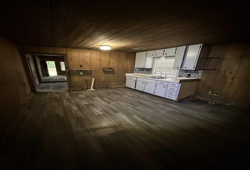 Kitchen area featuring wood-finish flooring, white cabinetry, a stainless steel sink, and a tiled backsplash