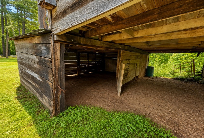 Rustic wooden barn structure with an open-air ground level, exposed timber framing, and a natural earth floor