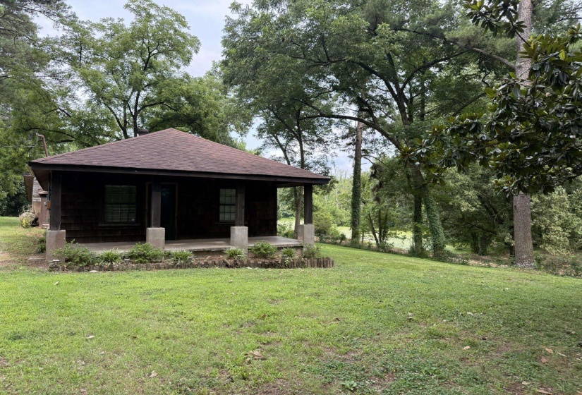 Charming cabin with a covered front porch featuring concrete pillars, a gabled roof, and wood-paneled siding