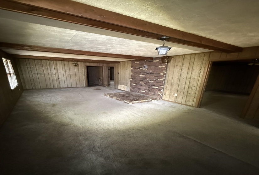 Room featuring exposed wood beams and a central brick fireplace with a raised hearth