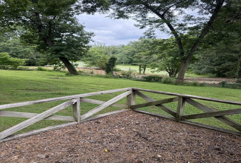 Terraced outdoor area with natural wood railing, overlooking a verdant landscape with mature trees and a tranquil water feature