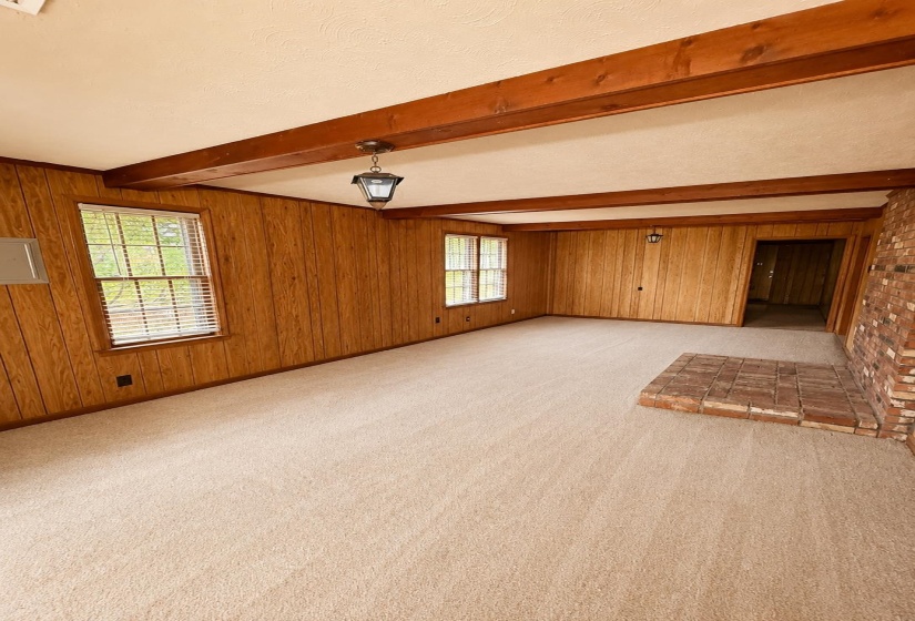 Spacious room with wood paneling, exposed wood ceiling beams, and light-toned carpeting
