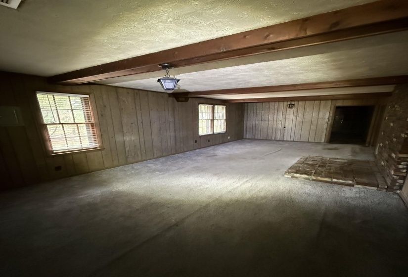 Spacious room featuring exposed wood ceiling beams, vertical wood paneling, a brick-surround hearth, and multiple windows with blinds