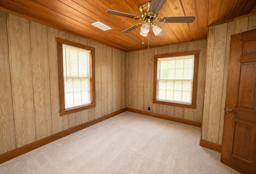 Room featuring two windows with blinds, wood-paneled walls, wood-finish ceiling, light-colored carpeting, and a ceiling fan with integrated lighting